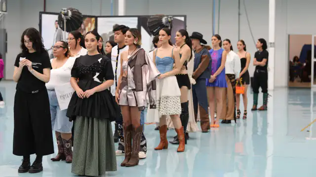 Personas en un evento de moda con prendas y artesanías sobre mesas, en un espacio iluminado.